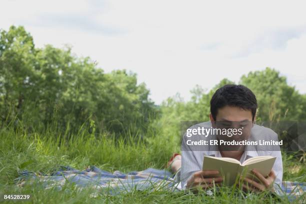 asian man laying on blanket reading book - saia midi stock-fotos und bilder