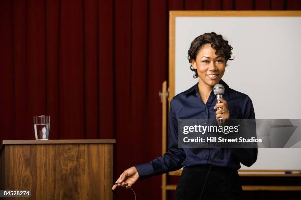 mixed race businesswoman speaking on stage - microphone debate stock pictures, royalty-free photos & images