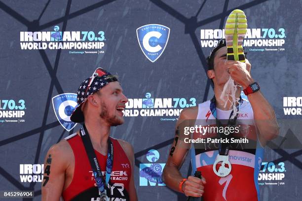 Ben Kanute of the USA watches Javier Gomez of Spain as he drinks champagne from a running shoe as they celebrate on the podium after the IRONMAN 70.3...