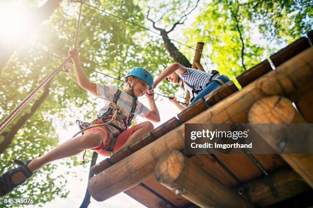 niña ayudando a su hermano en cuerdas - zip line fotografías e imágenes de stock