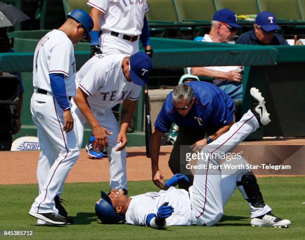 Texas Rangers first base coach Hector Ortiz , manager Jeff Banister and a trainer check on center fielder Carlos Gomez after he rolled his right...