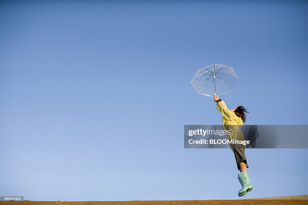 Young woman in raincoat holding polka-dot umbrella, jumping