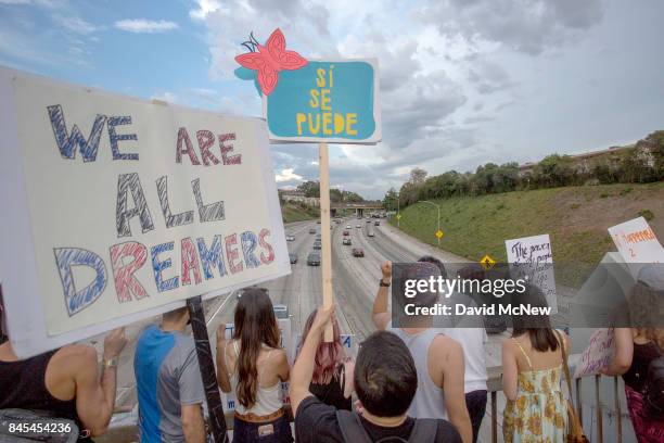 People hold signs over the 110 freeway as thousands of immigrants and supporters join the Defend DACA March to oppose the President Trump order to...