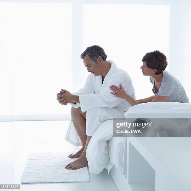 man sitting on edge of bed, wife consoling him - erectile dysfunction stock pictures, royalty-free photos & images