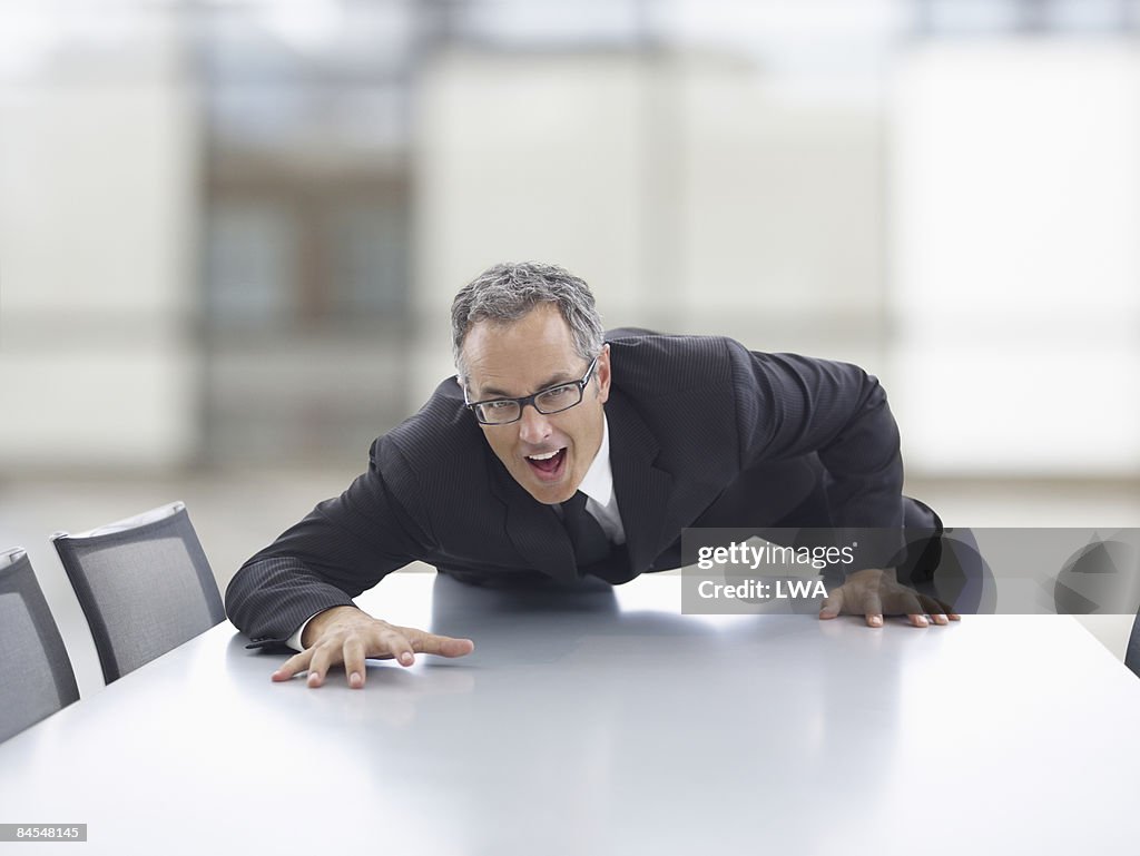 Businessman Climbing Across Conference Table