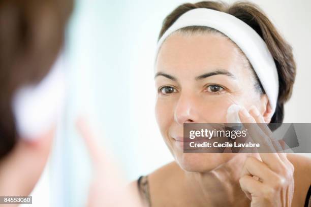 woman applying face cream in front of mirror - cream for face stock pictures, royalty-free photos & images