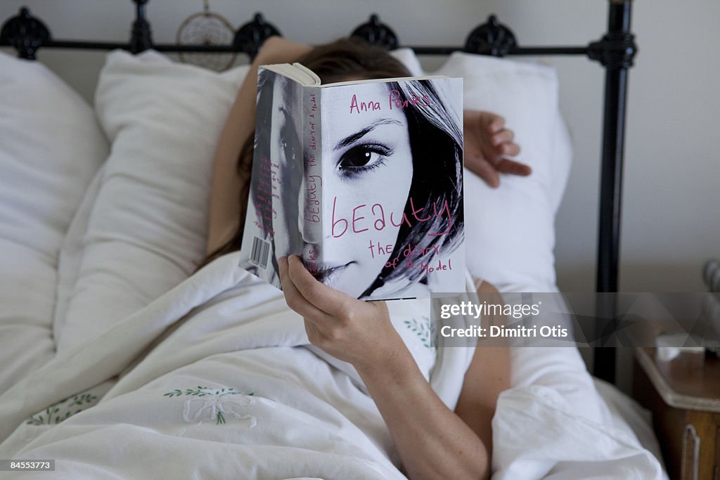 Woman reading in bed with book covering her face