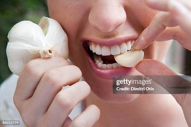 close up of woman biting into a garlic clove - woman look up stockfoto's en -beelden
