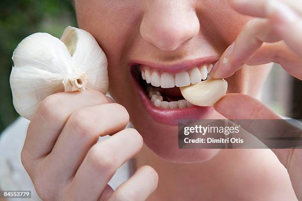 close up of woman biting into a garlic clove - knoflook stockfoto's en -beelden