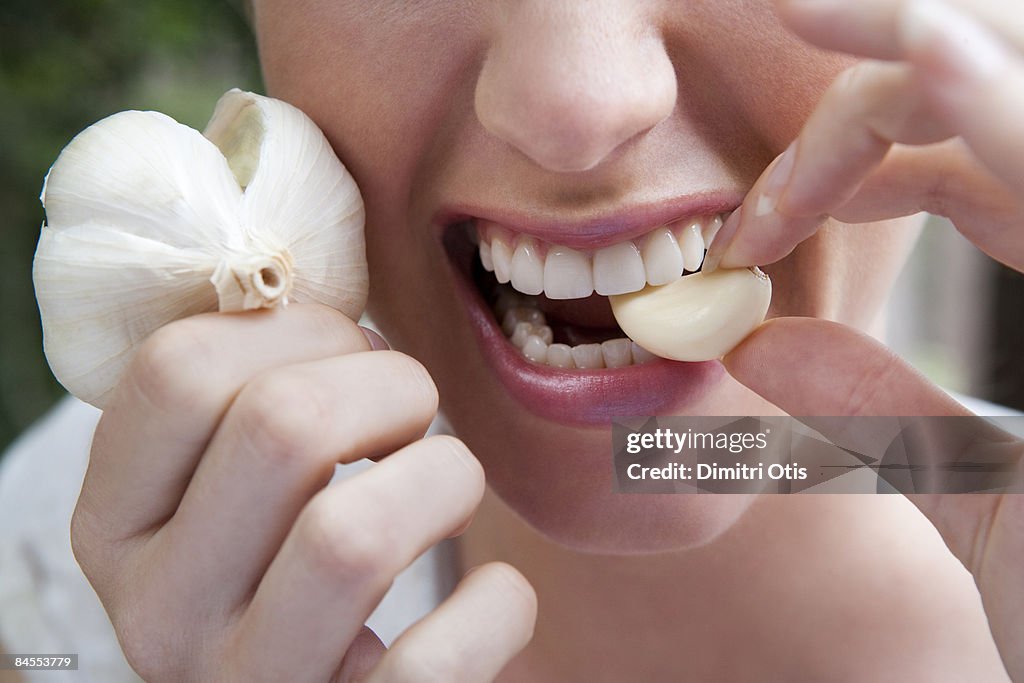 Close up of woman biting into a garlic clove