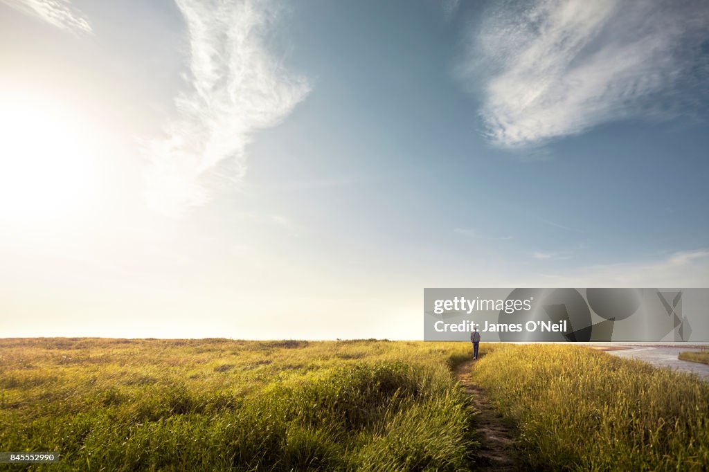 Man walking alone down country path at sunset