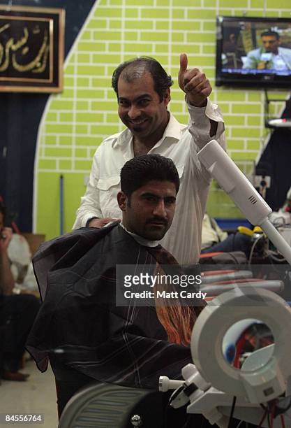 Barber gestures from his shop as he cuts a customer's hair on January 29, 2009 in Basra, Iraq. Many areas in Iraq are preparing for provincial...
