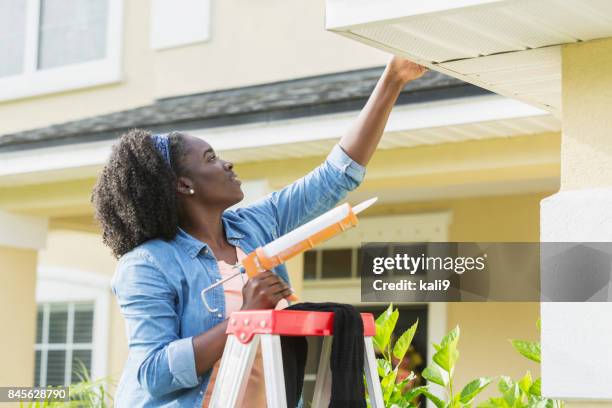 woman on ladder outside house doing repairs - new home exterior stock pictures, royalty-free photos & images
