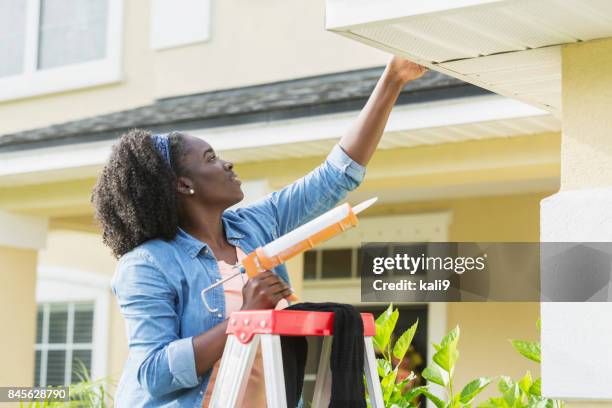 woman on ladder outside house doing repairs - caulk gun stock pictures, royalty-free photos & images