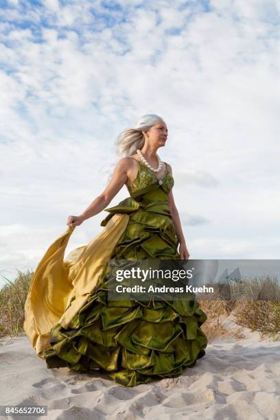 woman in her late fifties with long, silvery, grey hair blowing in the wind wearing an evening gown at the beach. - wavy hair beach stock pictures, royalty-free photos & images