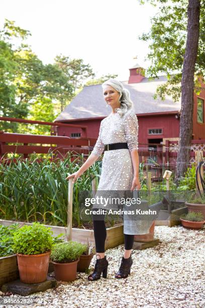 beautiful woman in her late fifties with long, silvery, grey hair wearing a fashionable outfit and high heels with a watering can in her vegetable garden. - formal garden fotografías e imágenes de stock