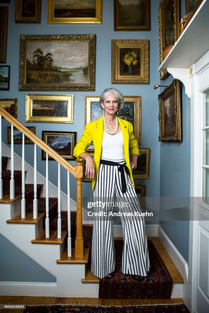 Beautiful woman in a fashionable outfit with silvery, grey hair standing in a staircase with golden framed oil painting on the wall.