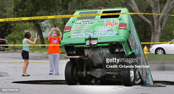 Residents take photos of a van remaining in a sinkhole on Monday, Sept. 11 that opened up at the Astor Park apartment complex in Winter Springs,...