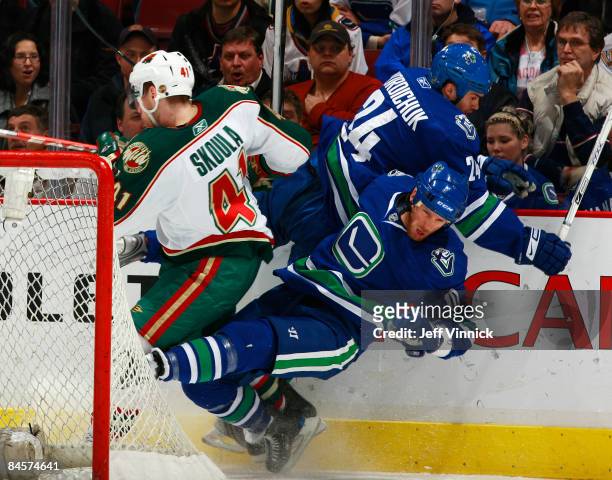 Ryan Johnson of the Vancouver Canucks and Darcy Hordichuk hit Martin Skoula of the Minnesota Wild along the boards during their game at General...
