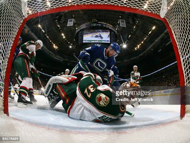 Niklas Backstrom of the Minnesota Wild tries to cover the puck with Henrik Sedin of the Vancouver Canucks watching over him in front of Martin Skoula...