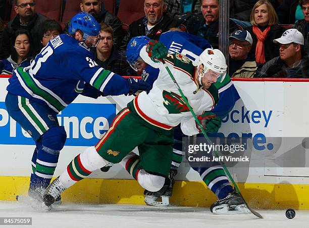 Andrew Brunette of the Minnesota Wild is knocked to the ice trying to get the puck from Henrik Sedin and Taylor Pyatt of the Vancouver Canucks during...