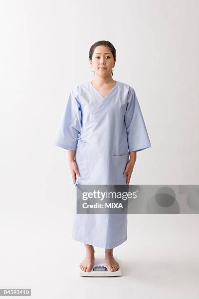 mid adult woman standing on bathroom scale - hospital gown stock pictures, royalty-free photos & images