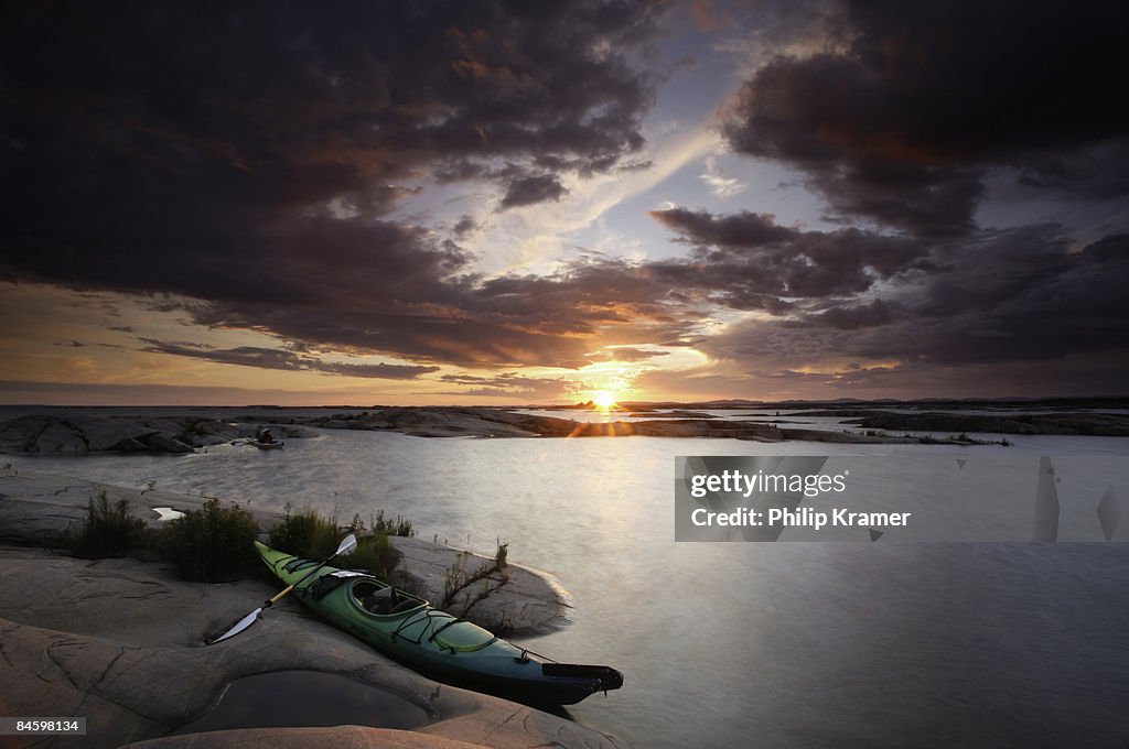 Kayak rests on rocks at sunset.