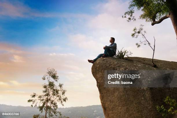 a man sitting on cliff enjoy the view - cliff side stock pictures, royalty-free photos & images