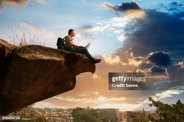 man standing at the edge of a cliff using laptop - at the edge of stock pictures, royalty-free photos & images