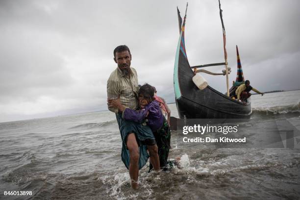 Rohingya man carries an elderly woman, after the wooden boat they were travelling on from Myanmar, which can be seen in the background, crashed into...