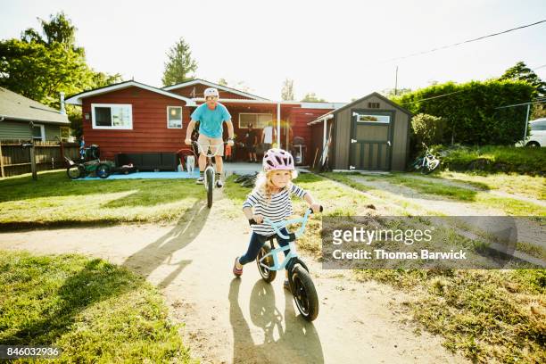 father and young daughter riding bmx bikes on dirt track in backyard on summer afternoon - differential focus fotografías e imágenes de stock