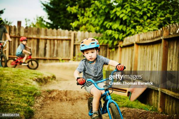 Young boy riding BMX bike on backyard dirt track on summer evening