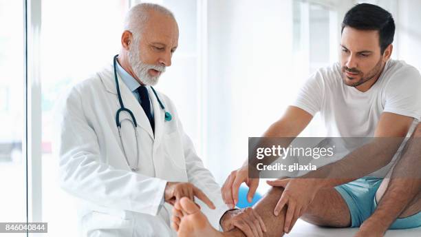 jonge man met zijn enkel onderzocht. - handsome doctors stockfoto's en -beelden