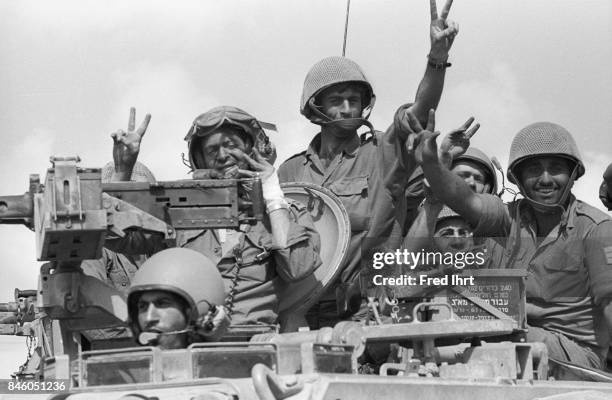 Israeli soldiers cheering and waving while driving by with their troops in tanks. On the Golan Heights during the Yom Kippur war.