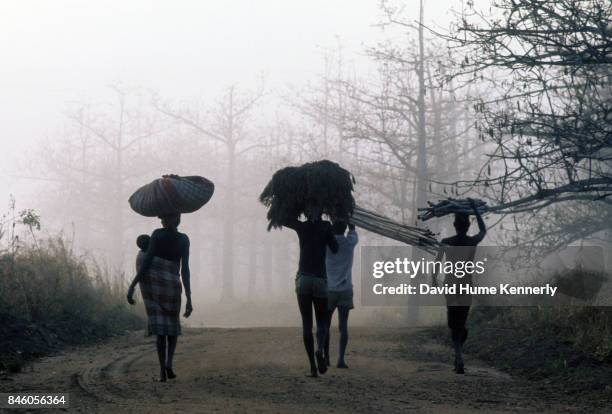 View of a group of people as they carry bundles on their heads and walk along a misty road, northern Mozambique, July 27, 1973.