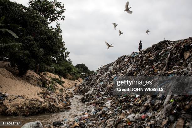 Young girl stands on a dirty river bank littered with garbage, on September 12, 2017 in the Ngaliema neighborhood in Kinshasa.