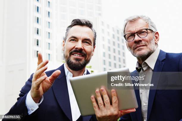 portraits of two businessmen standing in front of a modern apartment building - tablet 2 personen beratung stock-fotos und bilder