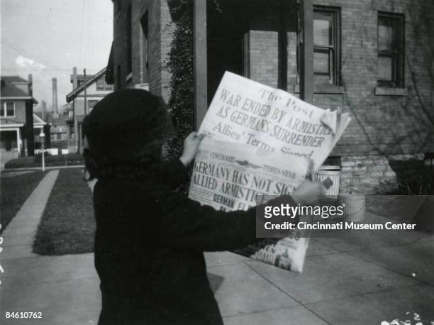 Woman reads the headlines of the local papers 'The Cincinnati Times Star' and 'The Post' proclaiming that an armistice has been signed ending the...