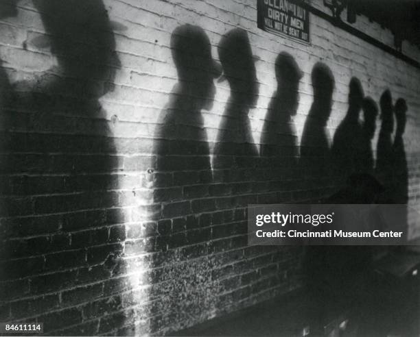 An atmospheric photo depicting shadows on a wall, Cincinnati, Ohio, 1930. The shadows belong to a group of men lined up for a bread line during the...