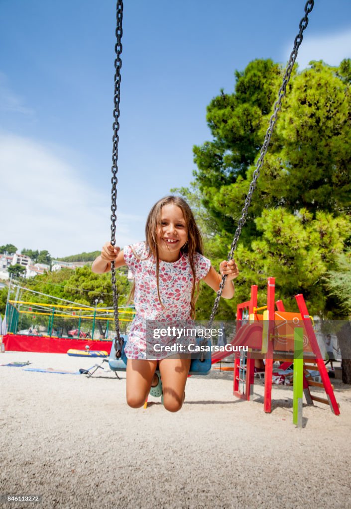 6 Years Old Joyful Girl On Beach Holiday Using Swing At The Playground