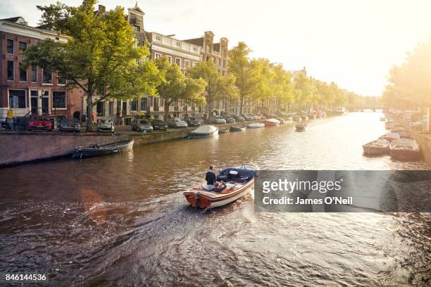 boat on a canal in amsterdam at sunset, netherlands - amsterdam mensen boot stockfoto's en -beelden