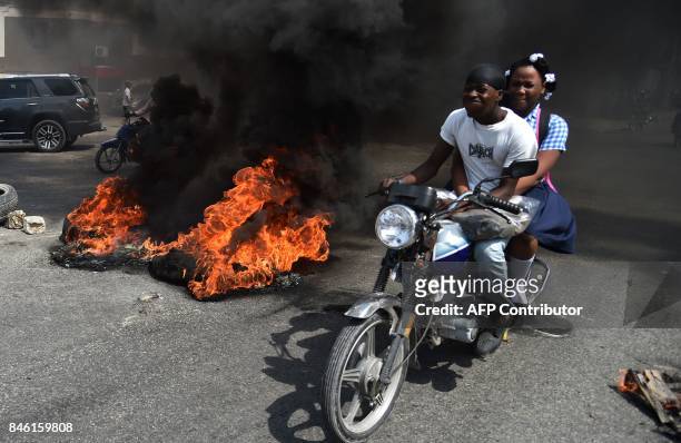Couple on a motorcycle drive past burning tires placed by demonstrators on a main road in the Haitian capital Port-au-Prince, on September 12, 2017....