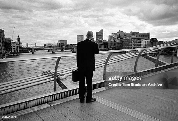 Business man pauses to take a call on Millennium Bridge over the River Thames, November 2008.