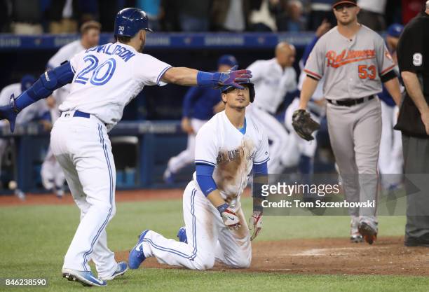 Darwin Barney of the Toronto Blue Jays is congratulated by Josh Donaldson after scoring on the game-winning run on an RBI single by Richard Urena in...