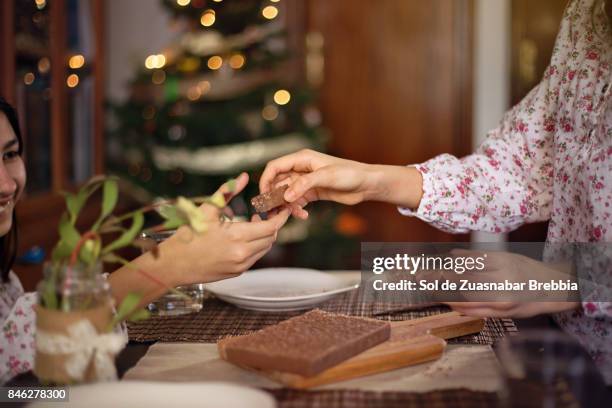 christmas. happy sisters sharing a chocolate nougat next to the christmas tree - kin in de hand stock-fotos und bilder