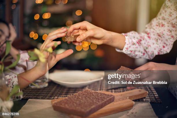 christmas. sisters sharing a chocolate nougat next to the christmas tree - kin in de hand stock pictures, royalty-free photos & images