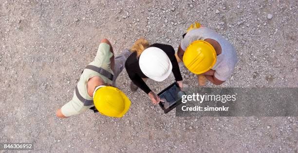 female architect and two construction workers checking plan on digital tablet and pointing at building to check progress - hard hat ipad stock pictures, royalty-free photos & images