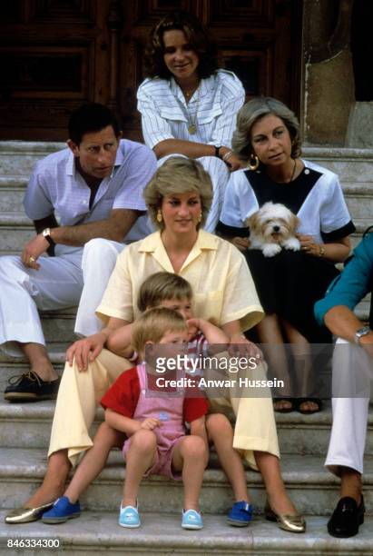 Prince Charles, Prince of Wales, Diana, Princess of Wales, wearing a yellow jumpsuit, Prince William and Prince Harry sit on the steps of Marivent...