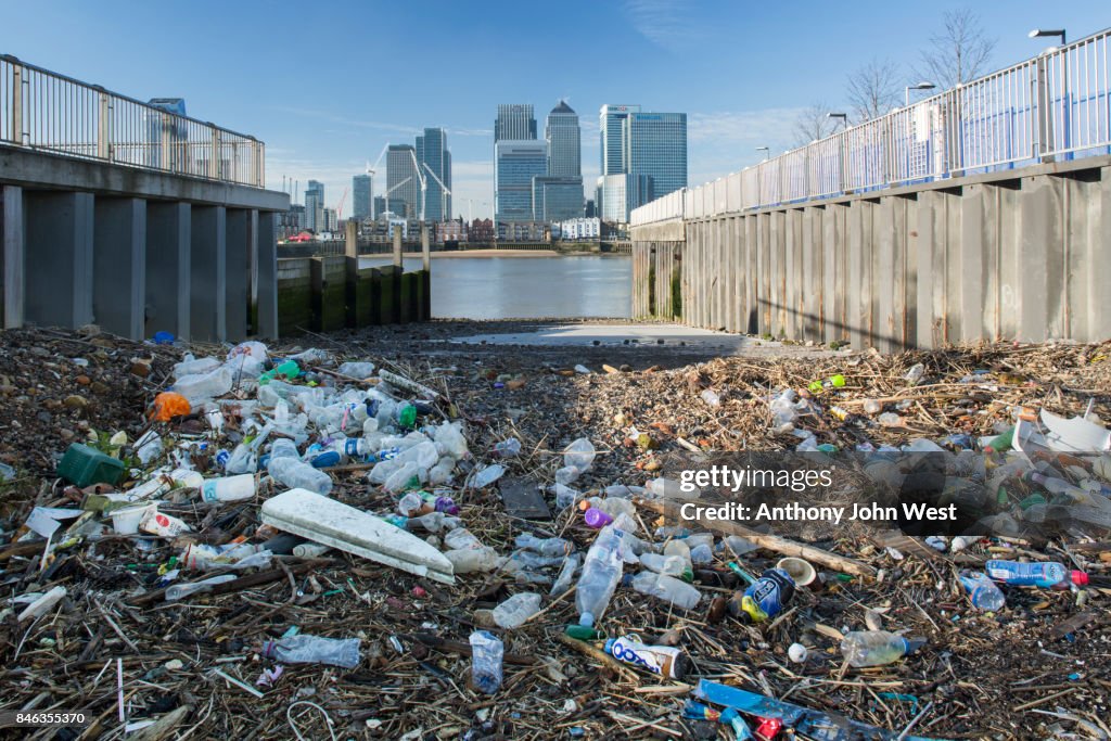 Garbage washed up by the tide opposite a skyline of International Banks, London