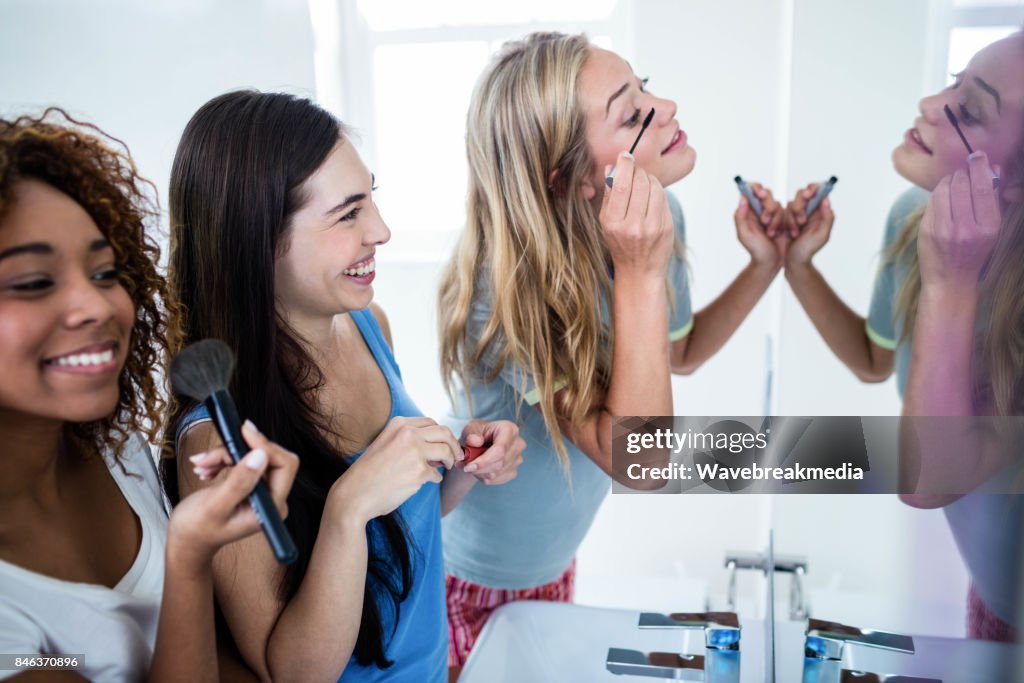 Three smiling friends putting makeup on together